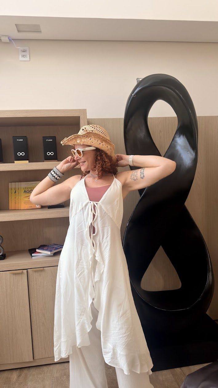 Jaya de branco e chapéu de palha ao lado de uma escultura preta